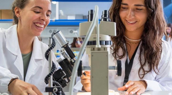dues noies al laboratori, treballant un microscopi